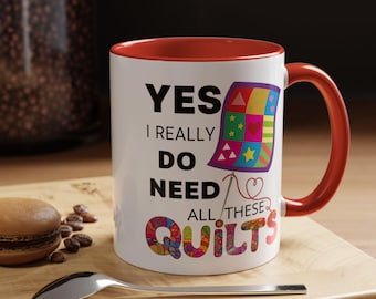 May include: White ceramic coffee mug with a red rim and handle. The mug has a black graphic that says "Yes I really do need all these quilts" with a colorful quilt design and a needle and thread.