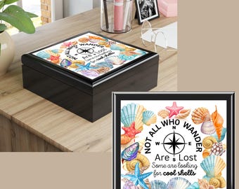 May include: Black keepsake box with a decorative lid featuring seashells, starfish, and a compass design. The text on the lid reads "Coastal Treasure Keepsake Box" and "Not All Who Wander Are Lost". A smaller framed image of the design is also shown.
