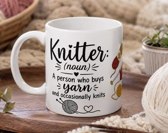 May include: White ceramic mug with the text "Knitter: (noun) A person who buys yarn and occasionally knits." The mug has a handle and a graphic of yarn and knitting needles. The mug is on a wooden tray.