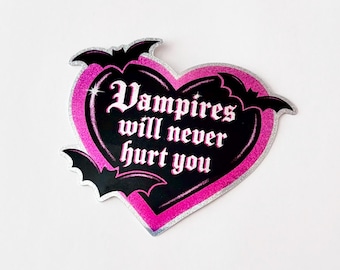 Könnte beinhalten: Ein herzförmiger Aufkleber mit schwarzem Zentrum und pinkfarbenem Glitzerrahmen. Der Aufkleber zeigt den Text "Vampires will never hurt you" in weißer gotischer Schrift mit schwarzen Fledermaus-Silhouetten.