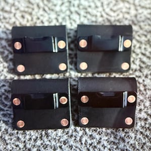 May include: Four black leather squares with copper rivets and a black rectangular accent. The squares are arranged in a grid pattern. The rivets are evenly spaced on each square.