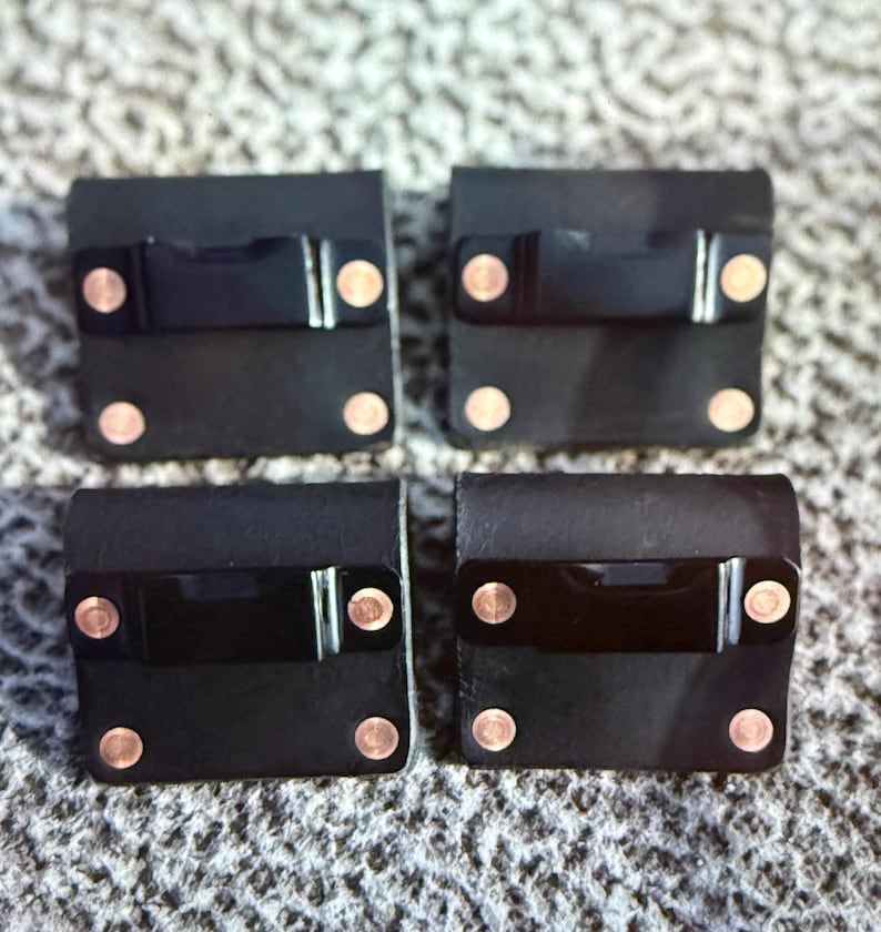 May include: Four black leather squares with copper rivets and a black rectangular accent. The squares are arranged in a grid pattern. The rivets are evenly spaced on each square.