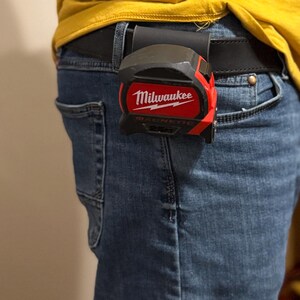 May include: A red and black Milwaukee 25 ft magnetic tape measure clipped to a black belt. The tape measure has the Milwaukee logo in white. The tape measure is attached to a black leather belt loop.