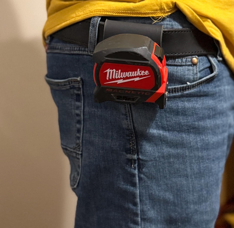 May include: A red and black Milwaukee 25 ft magnetic tape measure clipped to a black belt. The tape measure has the Milwaukee logo in white. The tape measure is attached to a black leather belt loop.