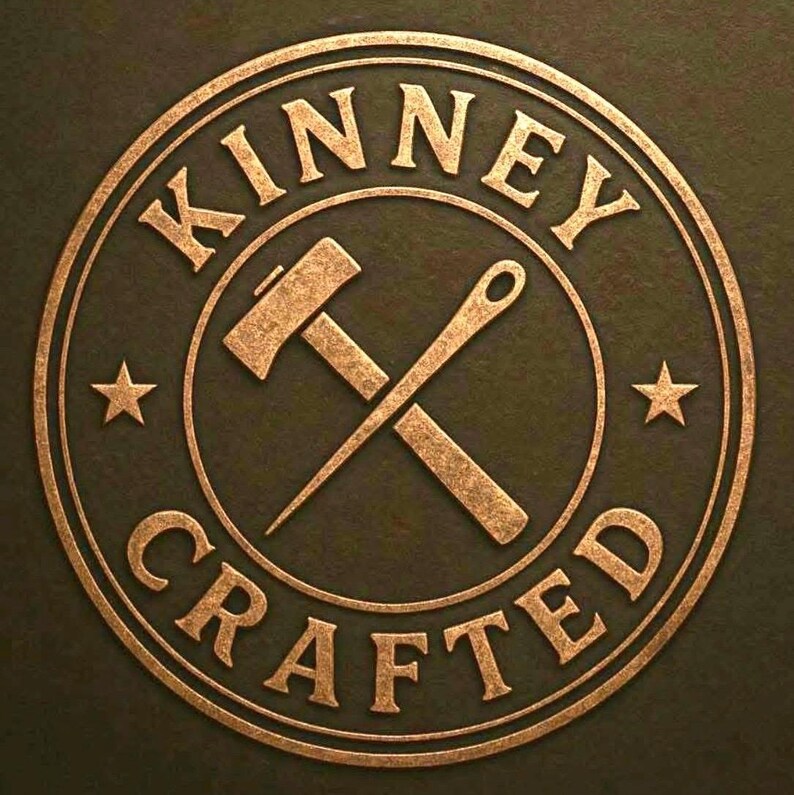 May include: Circular logo with the words "KINNEY CRAFTED" in a gold, embossed font. The logo features a hammer and needle crossed in the center, with a star on either side. The background is a dark olive green.