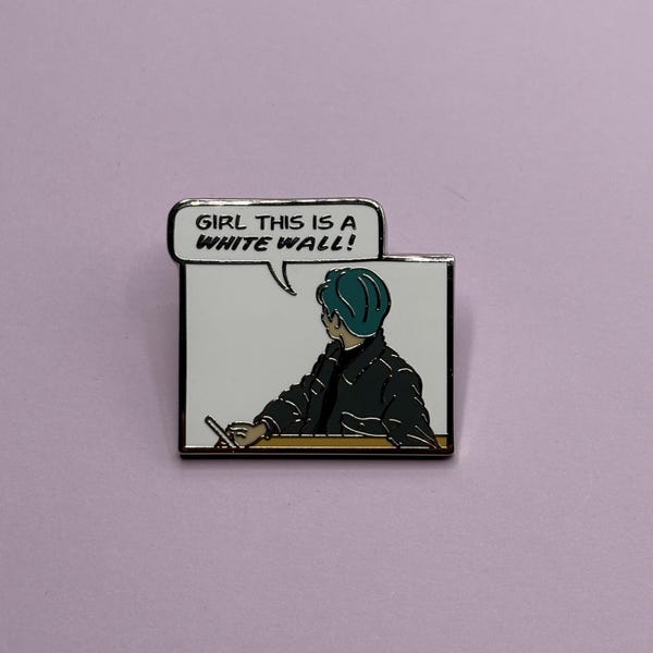 May include: A rectangular enamel pin featuring a comic-style illustration of a person with teal hair wearing a dark jacket. A speech bubble above the figure contains the black text, GIRL THIS IS A WHITE WALL! The pin has a white background.