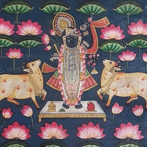 K&ouml;nnte beinhalten: Ein Gem&auml;lde, das eine hinduistische Gottheit, Krishna, darstellt, der auf einer Plattform mit zwei K&uuml;hen steht. Krishna ist mit aufwendigen Schmuck und Kleidung geschm&uuml;ckt und h&auml;lt eine Fl&ouml;te. Der Hintergrund ist dunkelblau mit Lotusblumen und Bl&auml;ttern.