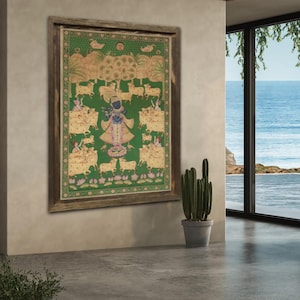 May include: A framed, colorful artwork depicting a religious scene with figures, cows, and trees on a green background. The artwork is in a wooden frame and hangs on a neutral-colored wall. A potted cactus sits nearby.