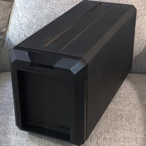 May include: A black rectangular storage box with the text "XPG SSD" on the front. The box has a geometric design with a textured finish on the corners and a recessed top. The bottom right corner has the text "Made for".