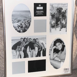 May include: A silver-toned multi-opening collage picture frame with a white mat. It features various rectangular and oval cutouts, including pre-inserted black and white photographs of a beach, three dogs, a group of six people, and one person.