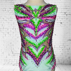 May include: A sleeveless gymnastics leotard in a light teal colour, adorned with a vibrant pattern of pink, purple, green, and gold embellishments. The leotard features a scoop neckline and is covered in sparkling rhinestones. The text "@rgleotards_by_ira" is visible at the top.