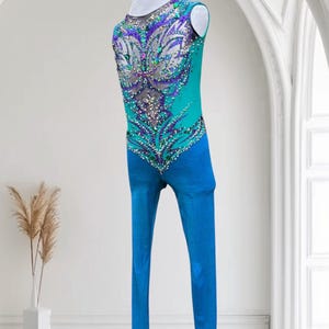 May include: A teal and blue leotard with intricate sequin and rhinestone embellishments. The leotard features a butterfly-like design on the back and sleeves. The text "1-2 weeks production" is visible at the bottom.
