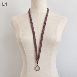 May include: A long lanyard featuring a gathered, ruched fabric strap in a muted mauve colour. The strap is attached to a silver-toned metal charm shaped like a five-petaled flower. The text L1 is visible in the upper left corner of the image.