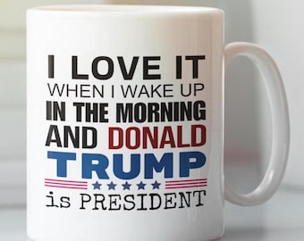 May include: White ceramic coffee mug with a black and red design. The text on the mug reads "I love it when I wake up in the morning and Donald Trump is President".