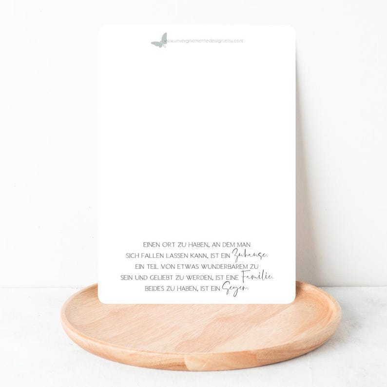 Peut inclure: Une carte blanche avec un motif de papillon gris en haut et une citation en allemand sur le fait d'avoir un foyer et une famille. La citation dit : "Einen Ort zu haben, an dem man sich fallen lassen kann, ist ein Zuhause. Ein Teil von etwas Wunderbarem zu sein und geliebt zu werden, ist eine Familie. Beides zu haben, ist ein Segen."