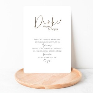 Peut inclure: Une carte marron avec le texte "Danke Mama & Papa" et un petit symbole de c&oelig;ur. La carte contient une citation sur l'importance de la famille et du foyer.