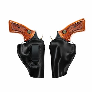 May include: Two revolvers with wooden grips are displayed, each in a black leather holster. The holsters have a clip for attachment. The revolvers have a polished finish and are set against a white background.