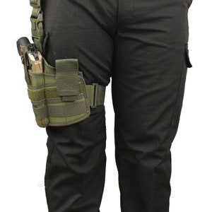 May include: A tactical leg holster in olive green, designed to secure a handgun. The holster features multiple compartments and straps for secure attachment to the leg and belt. The image shows the holster attached to a person's leg, with black pants.