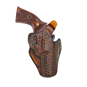 K&ouml;nnte beinhalten: Ein braunes Lederholster mit einem gewebten Korbgeflechtmuster, das einen Revolver mit einem Holzgriff h&auml;lt. Das Holster hat orangefarbene Akzente und schwarze N&auml;hte. Der Griff des Revolvers ist dunkelbraun mit einem goldenen Emblem.