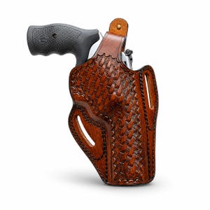 May include: A brown leather holster with a woven basketweave pattern, holding a black and silver revolver. The holster has a curved design with a belt loop and a cutout for the trigger. The leather is a rich, dark brown colour.