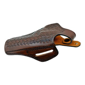 K&ouml;nnte beinhalten: Ein braunes Lederholster mit einem Korbgeflechtmuster. Das Holster hat ein gebogenes Design mit einer G&uuml;rtelschlaufe und einem Druckknopfverschluss. Das Leder ist dunkelbraun mit helleren braunen Akzenten.