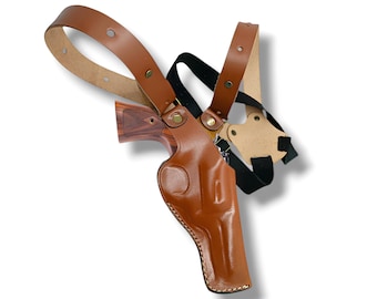 May include: A brown leather shoulder holster with a matching belt and straps. The holster is designed to hold a handgun, with a molded shape and stitching details. The straps are adjustable and connect with brass-colored hardware.