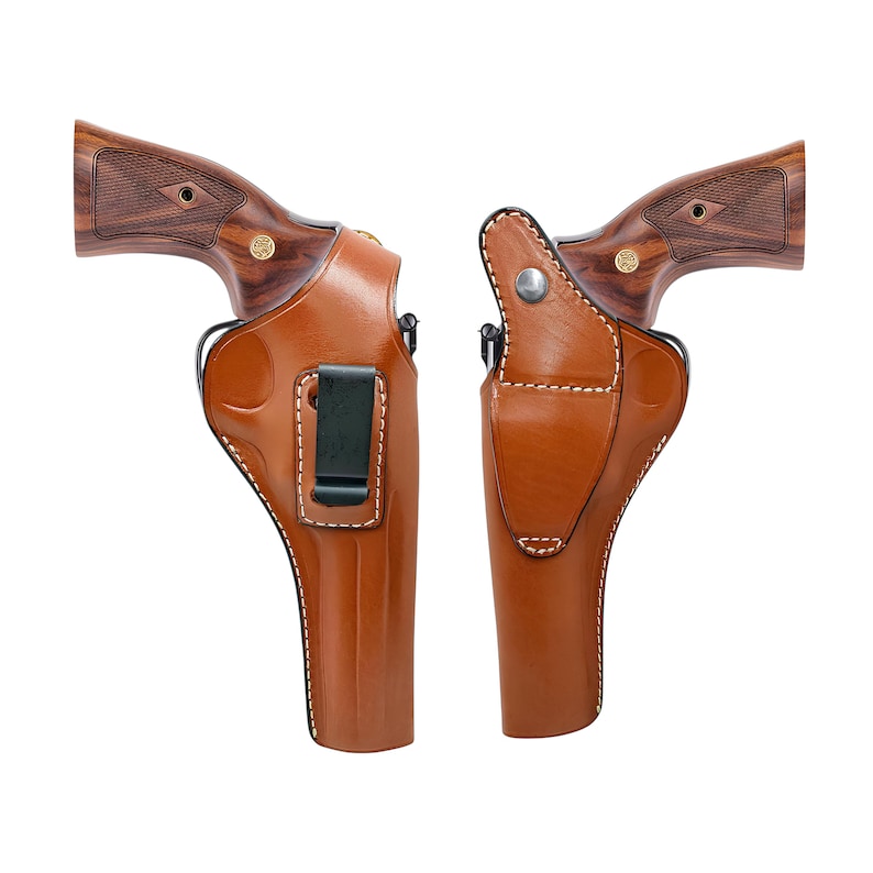 Op de afbeelding: Twee bruine leren holsters met witte stiksels en zwarte riemclips. De holsters zijn ontworpen om een ​​vuurwapen vast te houden. De handvatten van de vuurwapens zijn gemaakt van hout met een donker nerfpatroon.
