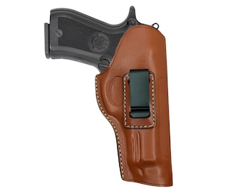Op de afbeelding: Een bruin leren holster met een zwart pistool erin. De holster heeft een zwarte metalen clip en witte stiksels. Het pistool is zwart met een getextureerde grip. De afbeelding staat tegen een witte achtergrond.