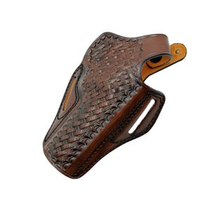 Pode incluir: Uma coldre de couro castanho com um padr&atilde;o de tecido de cesta. O coldre tem uma forma curva com um passador de cinto e um recorte para uma arma de fogo. O couro &eacute; de uma cor castanha escura rica.