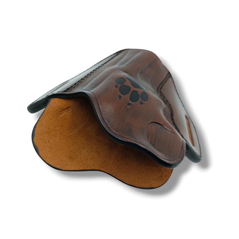 May include: A brown leather holster with a paw print design. The holster has a textured exterior and a tan interior. The edges are black and the holster is designed to hold a firearm.