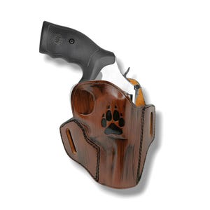 Könnte beinhalten: Ein braunes Lederholster mit einem schwarzen Pfotenabdruck-Design, das einen silbernen und schwarzen Revolver hält. Das Holster hat eine strukturierte Oberfläche und ist mit schwarzem Faden genäht. Der Griff des Revolvers ist schwarz.