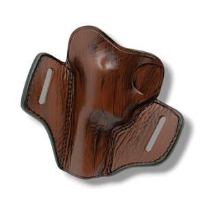 May include: A brown leather holster with a wood grain pattern. The holster has a molded shape with stitched edges and two slots for a belt. The leather is a rich, dark brown color.