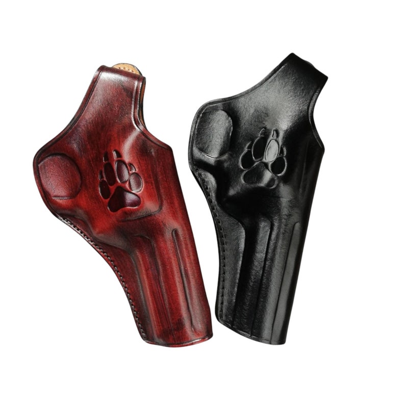 Peut inclure: Deux &eacute;tuis en cuir pour pistolet, un bordeaux et un noir, sont pr&eacute;sent&eacute;s sur fond blanc. Chaque &eacute;tui pr&eacute;sente un motif de patte d'animal. L'&eacute;tui bordeaux a un aspect textur&eacute;, tandis que l'&eacute;tui noir a une finition brillante.