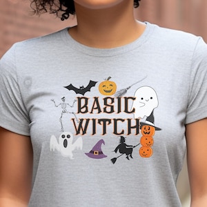 May include: A gray t-shirt with a Halloween-themed graphic that says "Basic Witch". The graphic includes a ghost, a witch, a skeleton, a bat, a pumpkin, and a witch's hat.