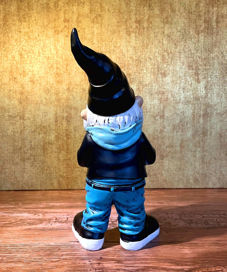 Peut inclure: Une figurine de gnome de jardin portant un chapeau noir, une &eacute;charpe bleue et un jean bleu. Le gnome est tourn&eacute; dos &agrave; la cam&eacute;ra et a une barbe blanche.