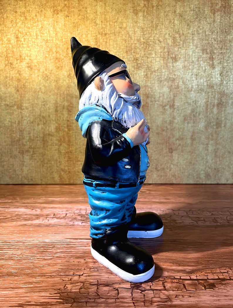 Peut inclure: Une figurine de gnome de jardin bleue et noire portant une veste en cuir, un jean bleu et des baskets noires. Le gnome a une barbe blanche et porte des lunettes &agrave; monture noire.
