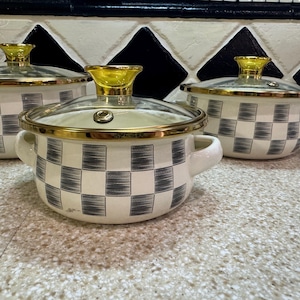 Könnte beinhalten: Drei Kochtöpfe mit weißem und grauem Schachbrettmuster, Glasdeckeln und goldenen Rändern. Jeder Topf hat einen goldenen Griff am Deckel und zwei weiße Griffe an den Seiten. Die Töpfe stehen auf einer gesprenkelten Arbeitsplatte.