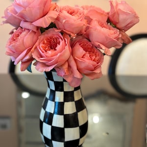 May include: A bouquet of pink roses in full bloom, arranged in a black and white checkered vase. The vase has a classic, curved shape. The roses have multiple layers of petals, and the overall effect is elegant and decorative.