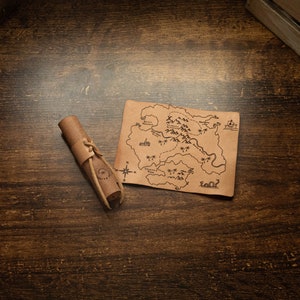 May include: A rolled-up leather map with a compass and a hand-drawn map of an island with trees and a river. The map is on a wooden table.