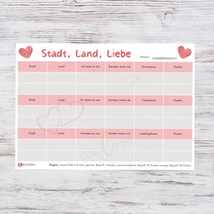 Puede incluir: Una hoja de juego rosa y gris con el texto alemán "Stadt, Land, Liebe" e ilustraciones de corazones. Dos almohadas blancas en forma de corazón con puntos azules están a cada lado de la hoja. La hoja tiene secciones para rellenar.