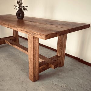 Könnte beinhalten: Ein rustikaler Holz-Esstisch mit natürlicher Holzoptik und einem schlichten, modernen Design. Der Tisch hat eine rechteckige Tischplatte und ein stabiles Gestell mit geometrischem Muster.