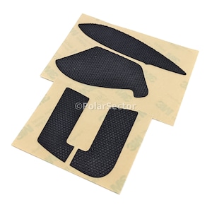 May include: A set of four black textured adhesive pads for a gaming controller. The pads are on a brown backing sheet with the 3M logo.