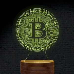 May include: A yellow illuminated 3D printed lamp shaped like a Bitcoin coin. The coin has the Bitcoin symbol in the centre and the text "BITCOIN DIGITAL DECENTRALIZED PEER TO PEER 1TROY OZ 999 FINE COPPER MJB MONETARY METALS" around the edge.