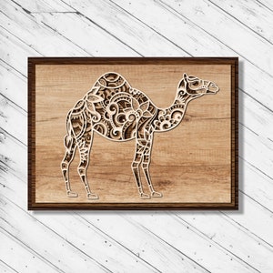 Può includere: Un pezzo di arte da parete in legno decorativo con un intricato design di cammello tagliato al laser. Il cammello è delineato in bianco su uno sfondo di legno marrone.