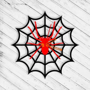 May include: A black spider web with a red spider in the center. The spider has eight legs and a round body. The web is made of thin black lines and is against a white wood background.