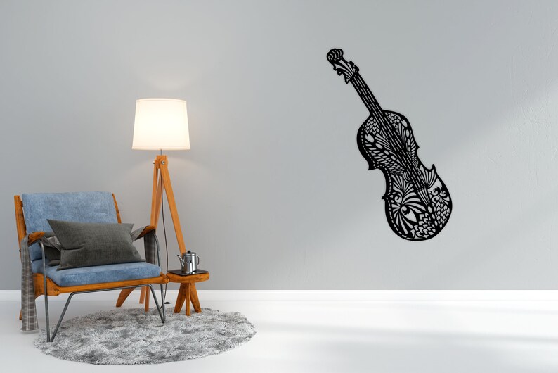 May include: A black and white patterned cello wall decor with intricate details. The cello is mounted on a white wall with a blue armchair and a lamp in the foreground.