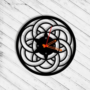 May include: Black clock with a circular design featuring overlapping circles. The clock face is black with white numbers and hands.