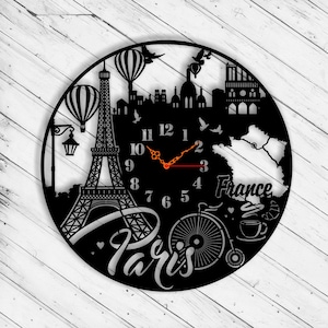 May include: Black and white clock with a Paris theme. The clock features the Eiffel Tower, hot air balloons, a bicycle, a cup of coffee, and the words "Paris" and "France".