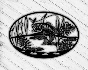 May include: Black metal wall art depicting a bass fish jumping out of the water with reeds and lily pads. The fish is in a circular frame.