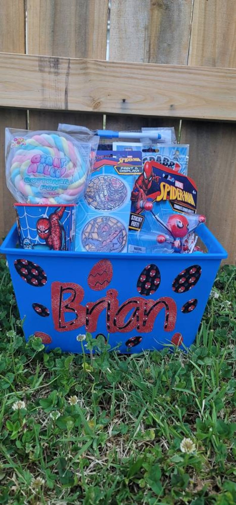 Puede incluir: Una cesta de pl&aacute;stico azul con tem&aacute;tica de Spiderman. La cesta tiene el nombre "Brian" escrito en rojo y negro en la parte delantera. La cesta est&aacute; llena de varios art&iacute;culos con tem&aacute;tica de Spiderman, incluyendo una pegatina de Spiderman, una impresi&oacute;n y una pantalla de Spiderman, un juguete de Spiderman con pies pegajosos y un algod&oacute;n de az&uacute;car de Spiderman.
